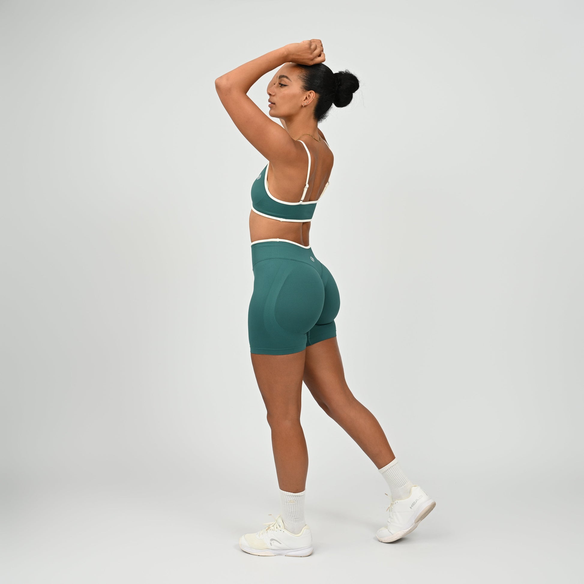 Hyrox athlete wearinga pair of Jade green booty shorts with white piping. High waisted with a cinch bum and contouring. Worn with a matching minimal sports bra. From the brand Hybryd.
