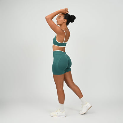 Hyrox athlete wearinga pair of Jade green booty shorts with white piping. High waisted with a cinch bum and contouring. Worn with a matching minimal sports bra. From the brand Hybryd.