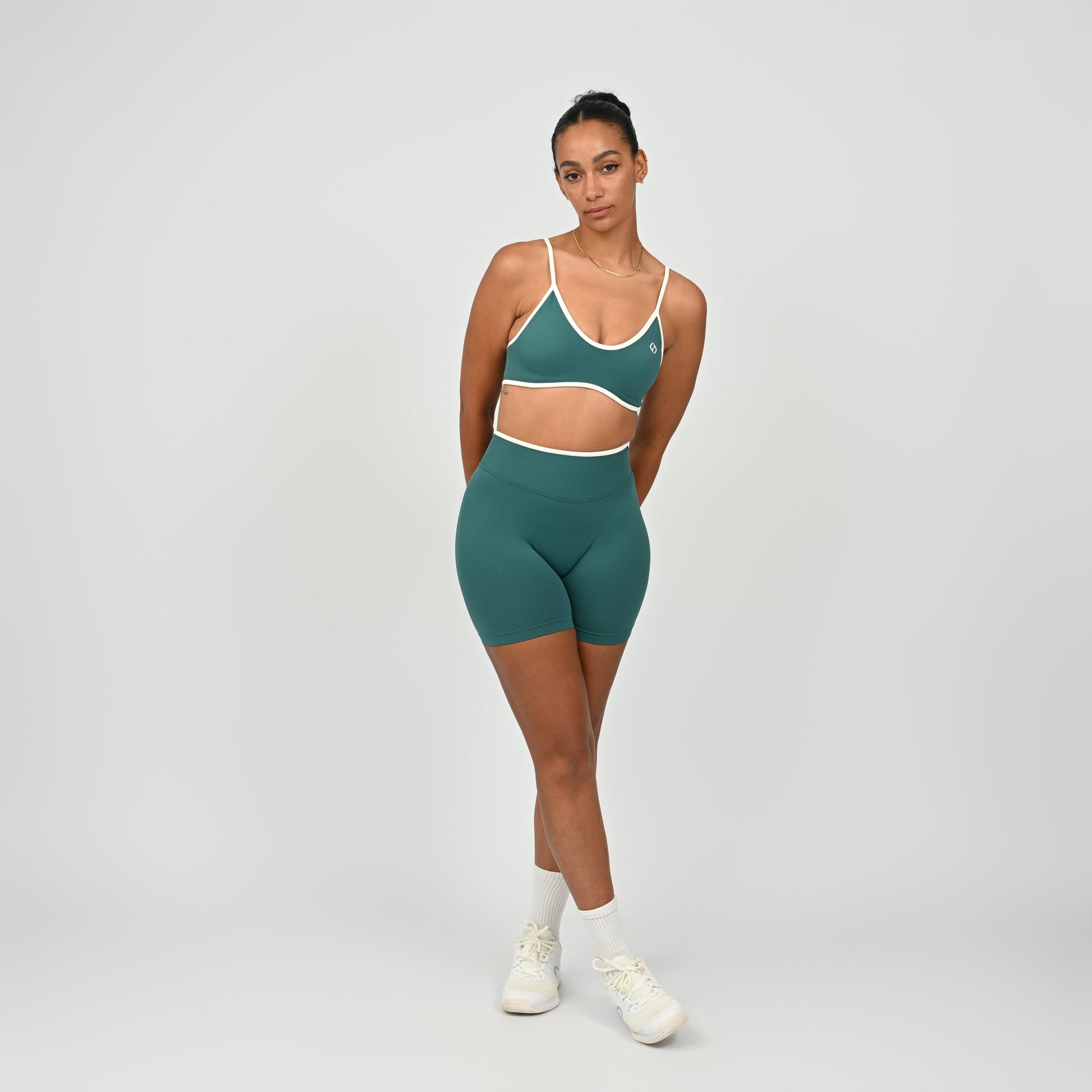 Hyrox athlete wearinga pair of Jade green booty shorts with white piping. High waisted with a cinch bum and contouring. Worn with a matching minimal sports bra. From the brand Hybryd.
