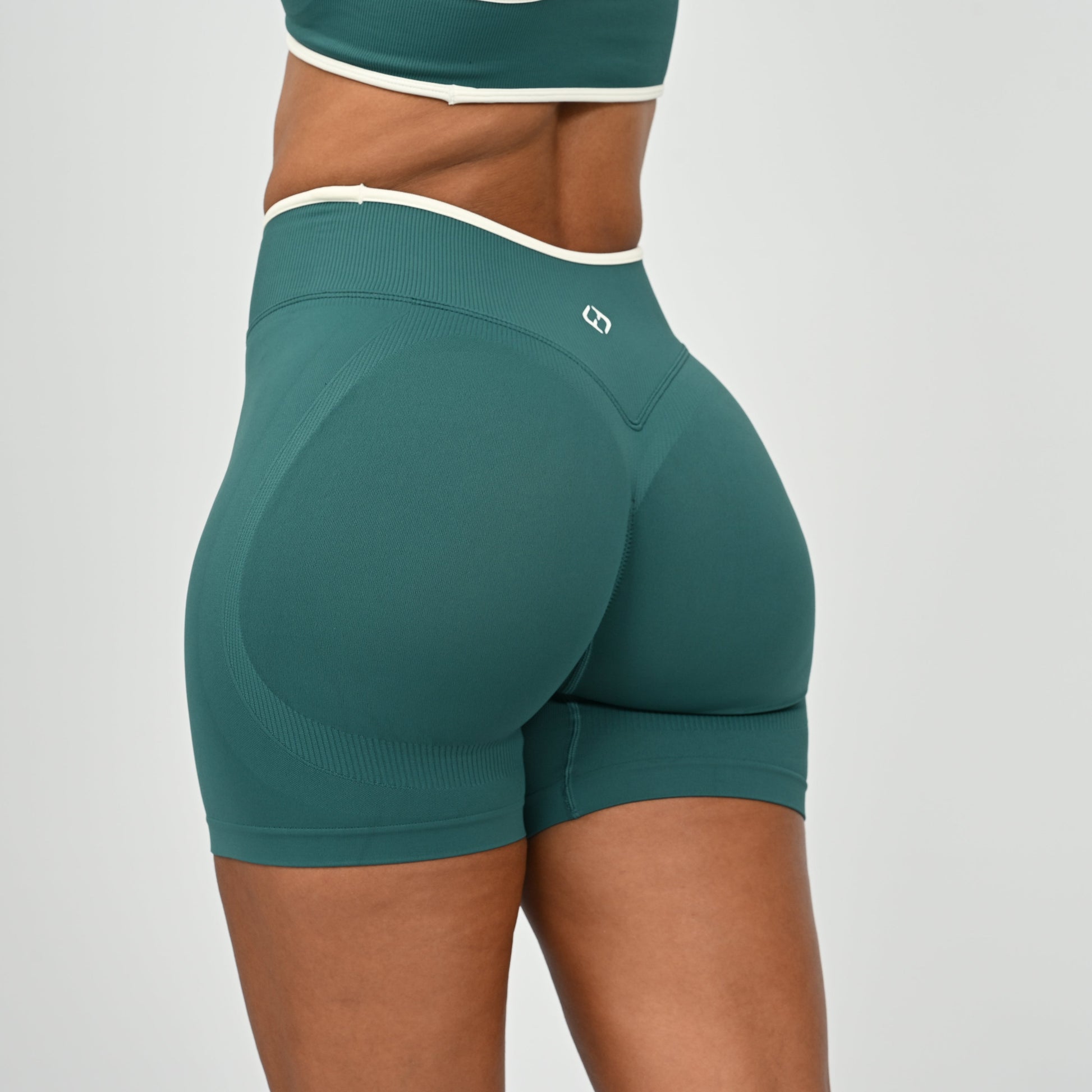 Hyrox athlete wearinga pair of Jade green booty shorts with white piping. High waisted with a cinch bum and contouring. From the brand Hybryd.