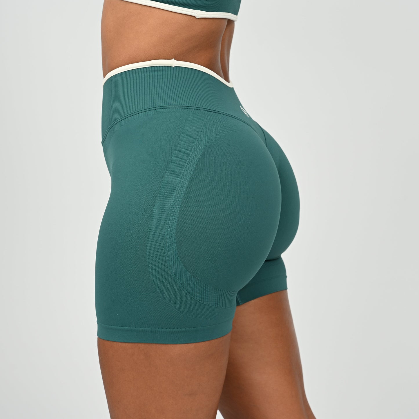 Hyrox athlete wearinga pair of Jade green booty shorts with white piping. High waisted with a cinch bum and contouring. From the brand Hybryd.