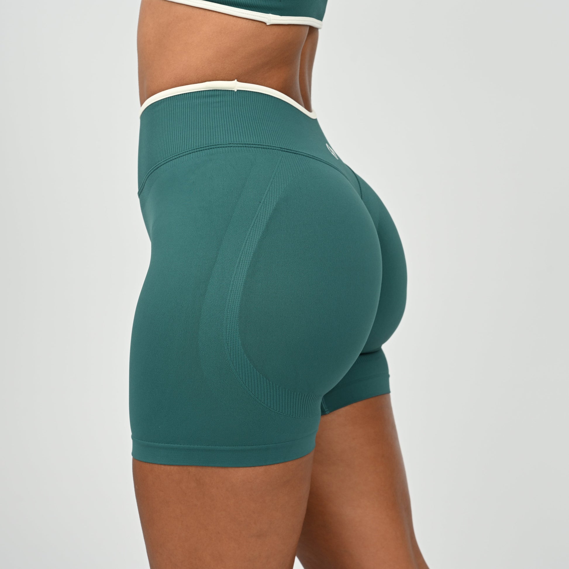 Hyrox athlete wearinga pair of Jade green booty shorts with white piping. High waisted with a cinch bum and contouring. From the brand Hybryd.