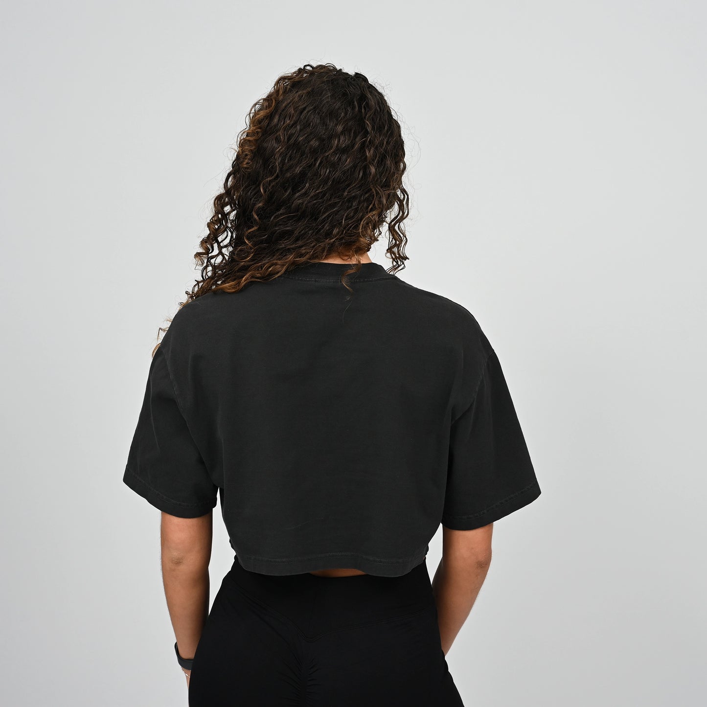 Person wearing a black Hybryd t-shirt from behind on a light grey background