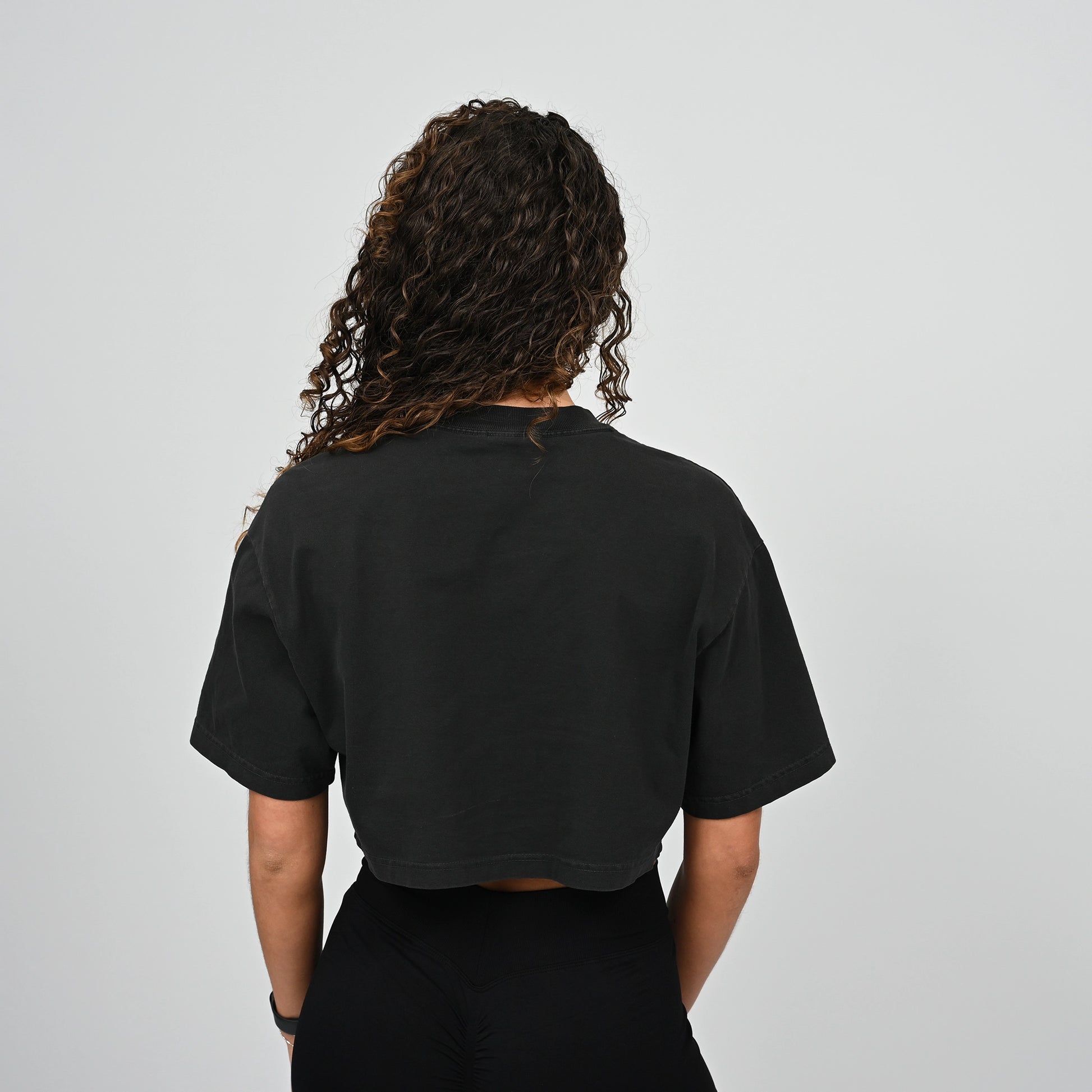 Person wearing a black Hybryd t-shirt from behind on a light grey background