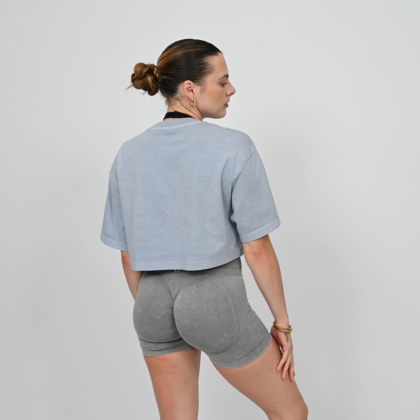 Woman wearing a blue cropped tee and grey scrunch bum shorts from the activewear brand Hybryd
