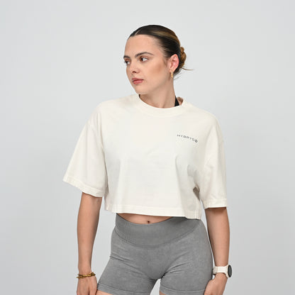 Woman wearing a white crop top and grey gym sorts from the brand Hybryd on a light grey background