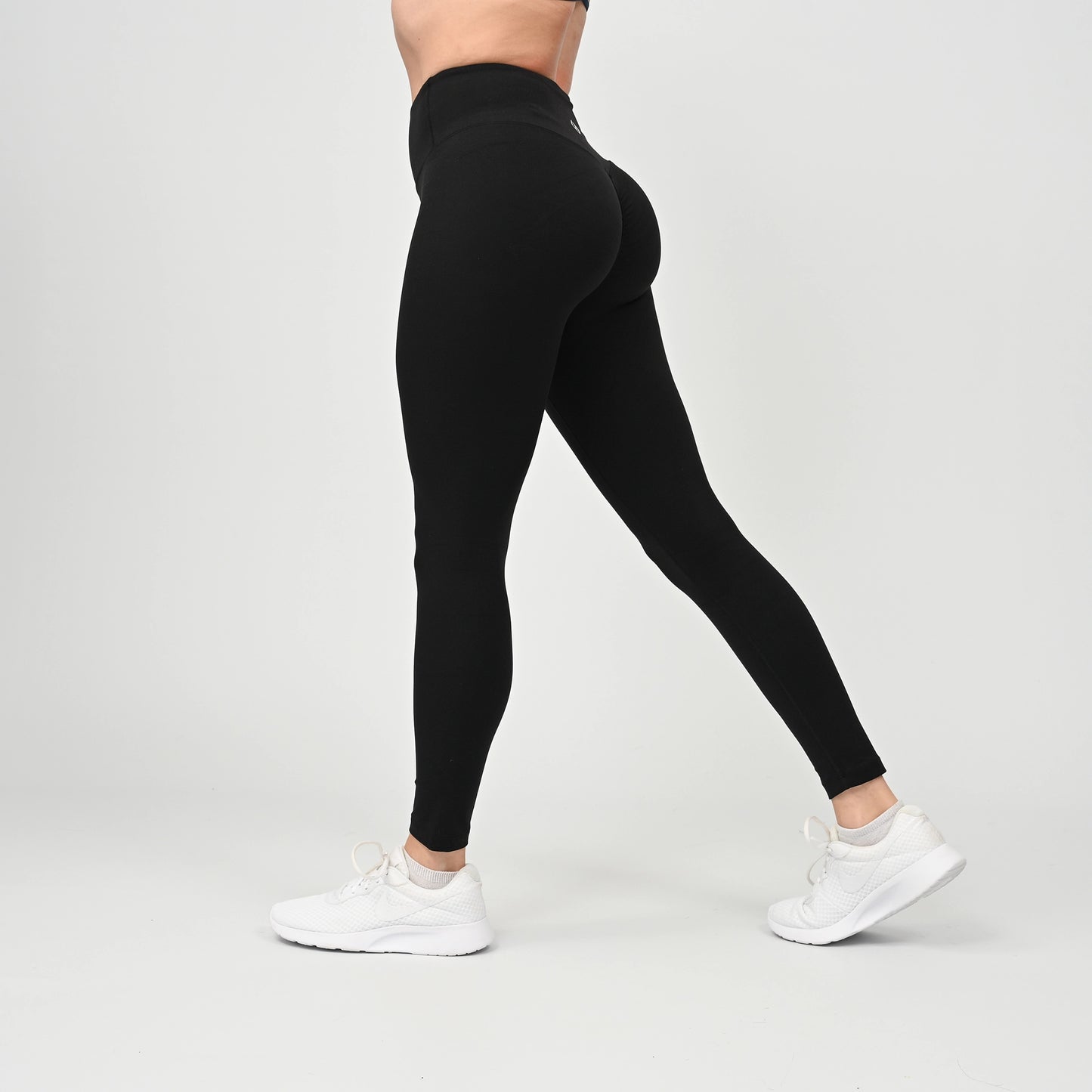 Person wearing black gym leggings with scrunch bum and white sneakers on a light gray background