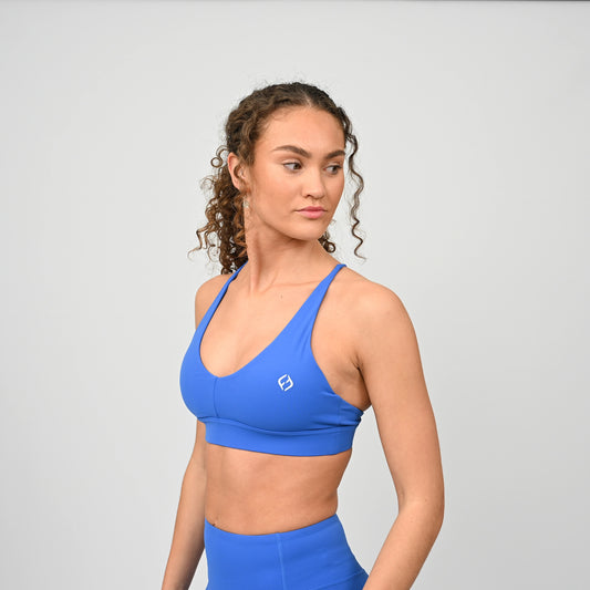Woman wearing a royal blue sports bra and leggings on a light gray background