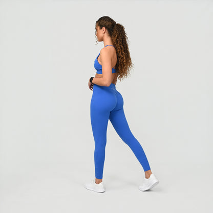 Woman wearing a blue crossfit gym athletic outfit with a bum scrunch on a light gray background