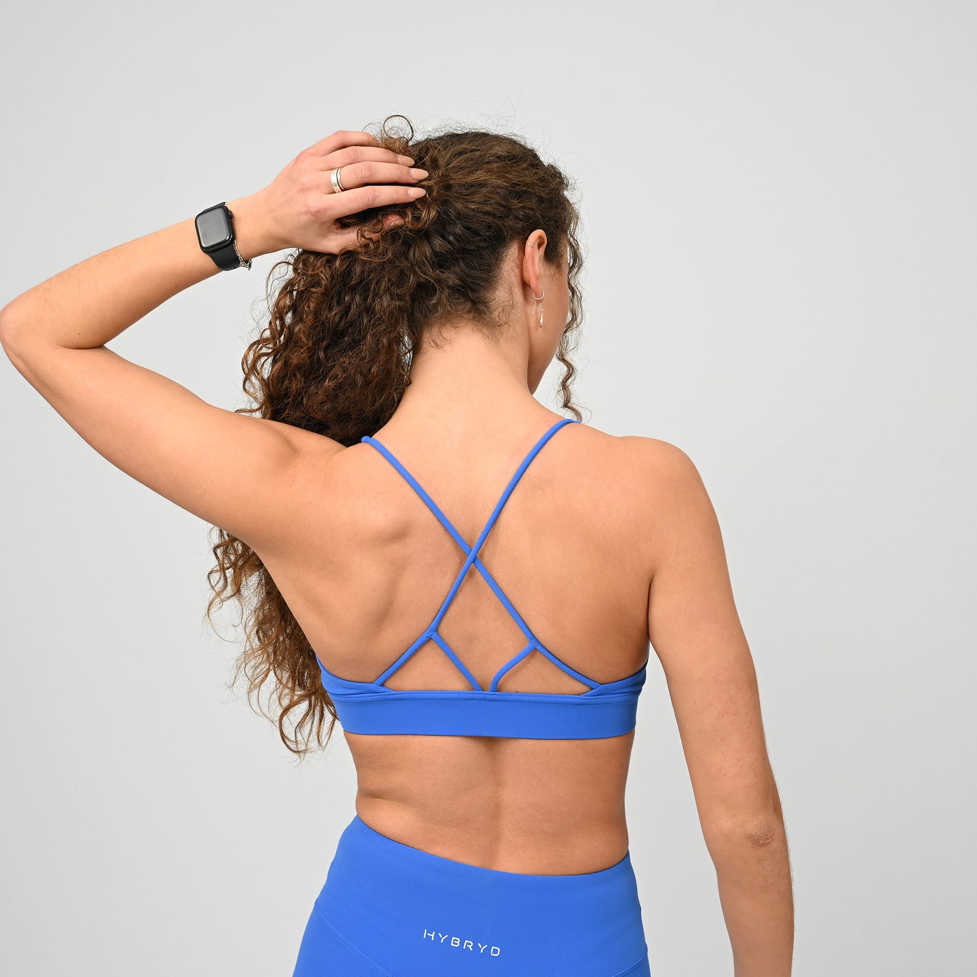 Woman wearing a blue minimal sports bra and leggings with 'HYBRYD' branding on a gray background