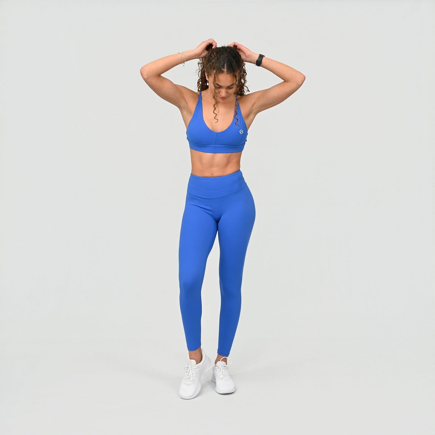 Woman wearing a blue workout athletic outfit with v-neck bra and high waist on a light gray background