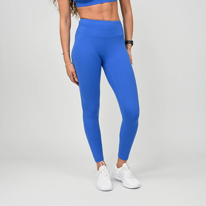 Person wearing blue high waisted leggings and white sneakers on a gray background