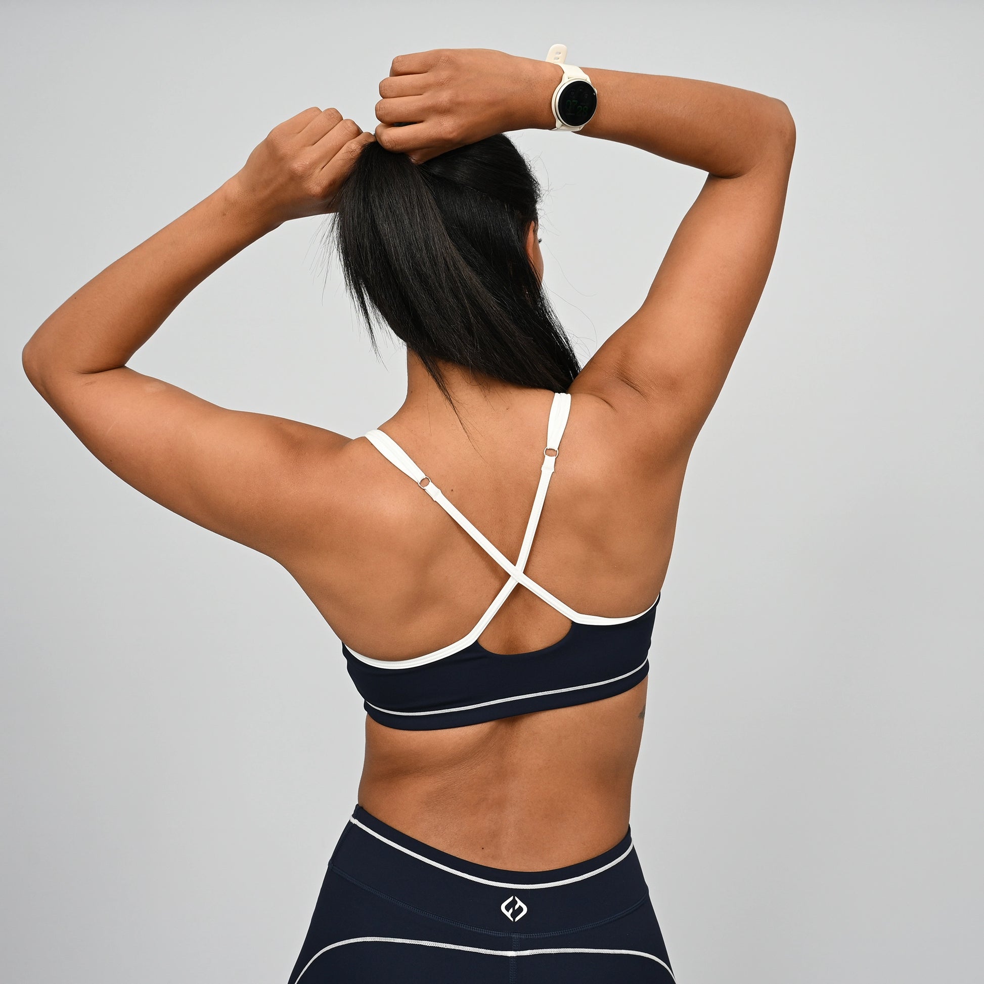 Female crossfit athlete wearing a navy minimal sports bra with white adjustable straps against a gray background from gymwear brand Hybryd