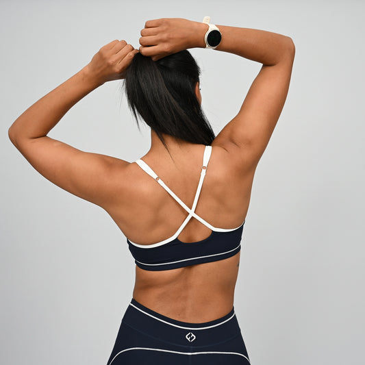 Female crossfit athlete wearing a navy minimal sports bra with white adjustable straps against a gray background from gymwear brand Hybryd