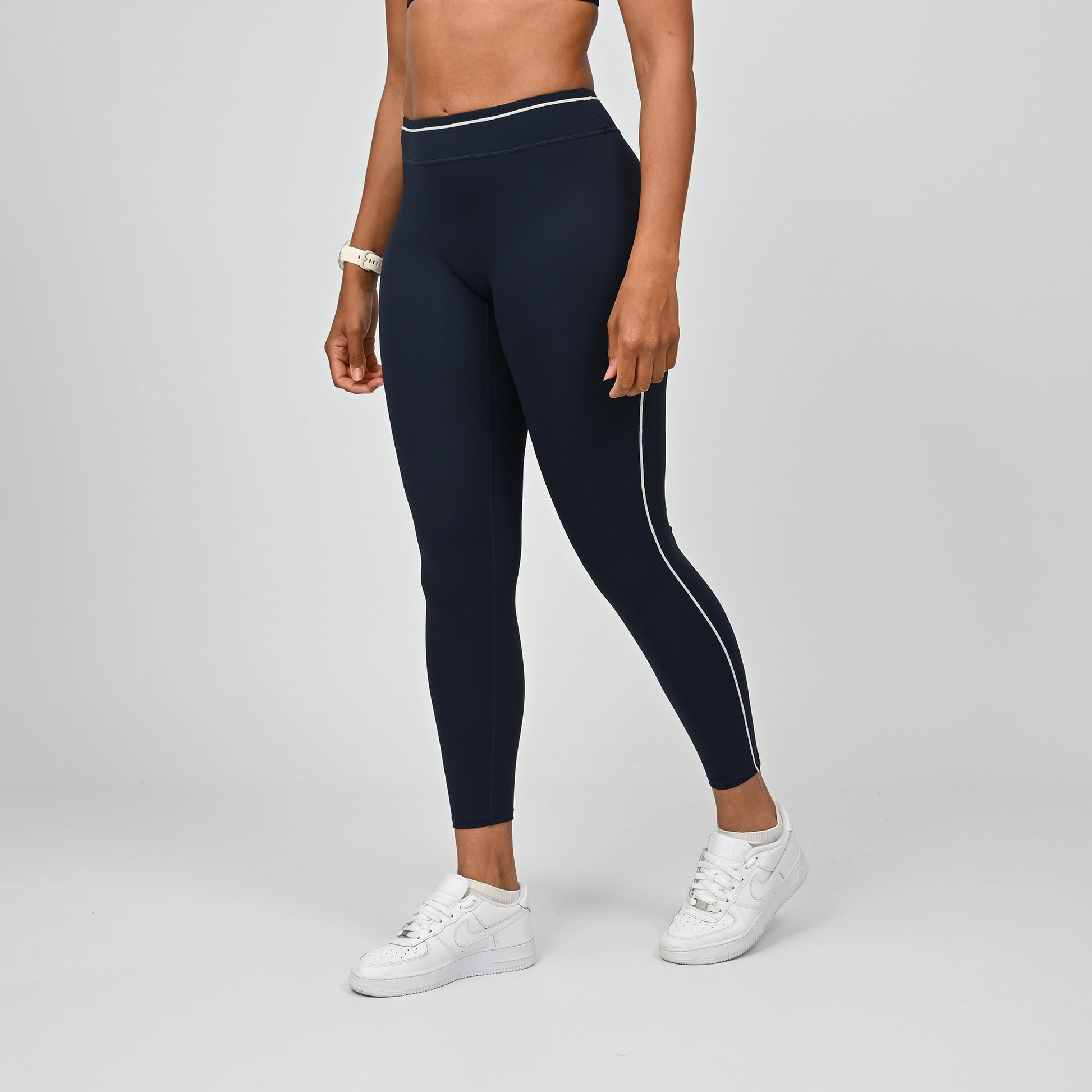 Hybrid yoga athlete wearing a rnavy crossfit gym outfit with white stripes on a gray background
