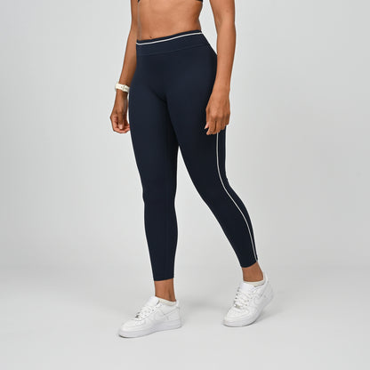 Hybrid yoga athlete wearing a rnavy crossfit gym outfit with white stripes on a gray background