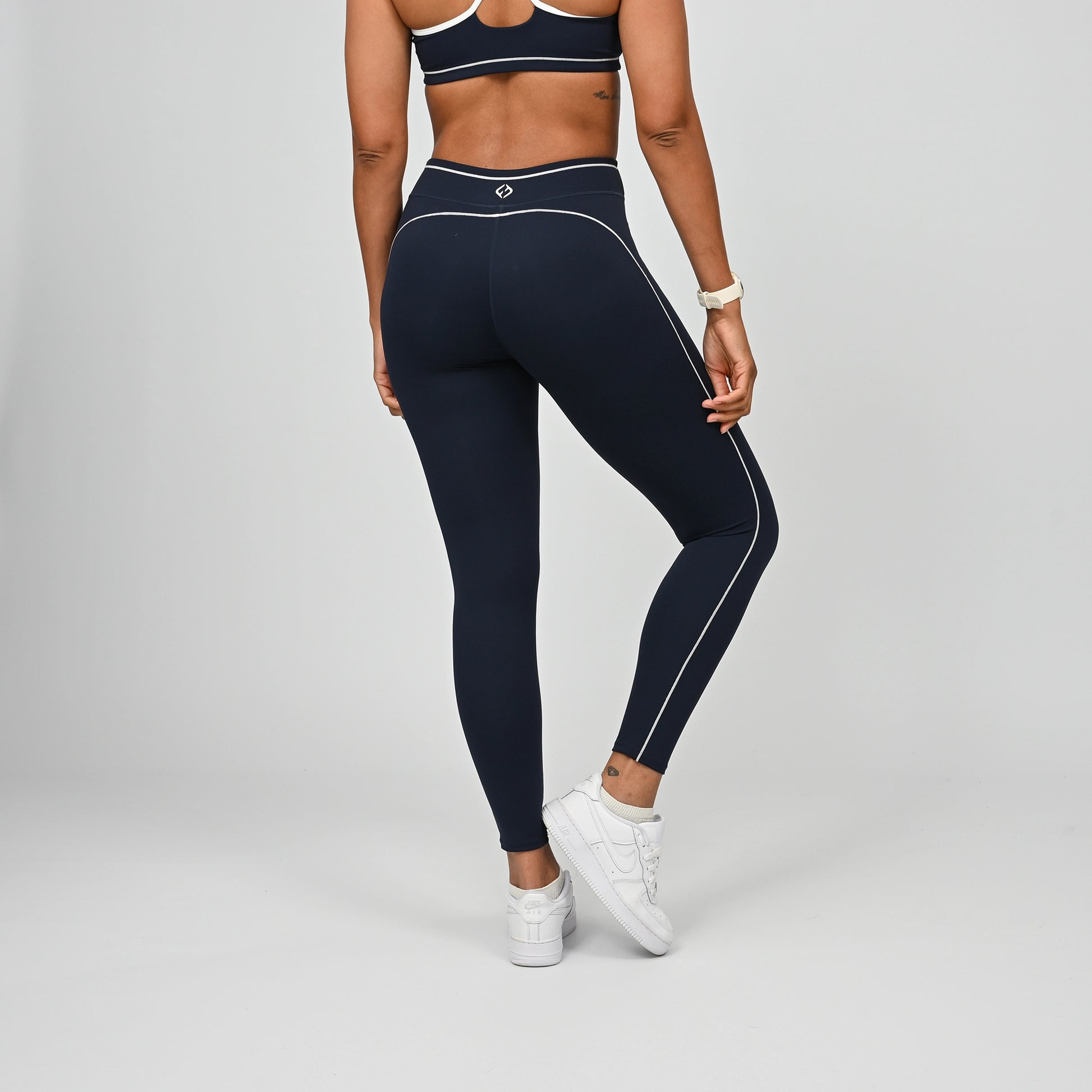 Hybrid yoga athlete wearing a navy crossfit gym outfit with white stripes on a gray background