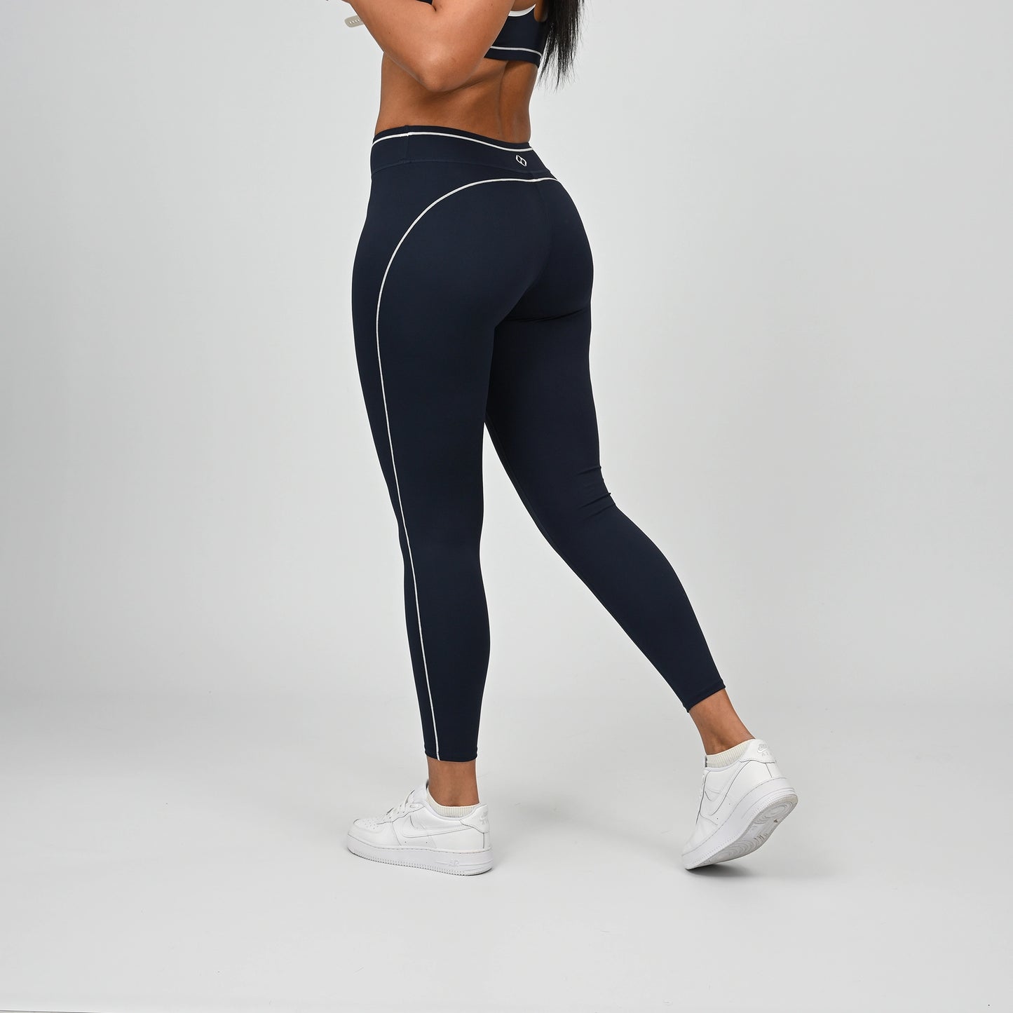 Hybrid yoga athlete wearing a rnavy crossfit gym outfit with white stripes on a gray background