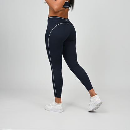 Hybrid yoga athlete wearing a rnavy crossfit gym outfit with white stripes on a gray background