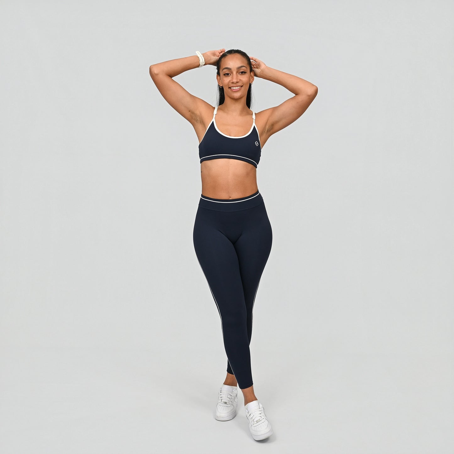 Female crossfit athlete wearing a Hybryd navy minimal sports bra with white adjustable straps against a grey background