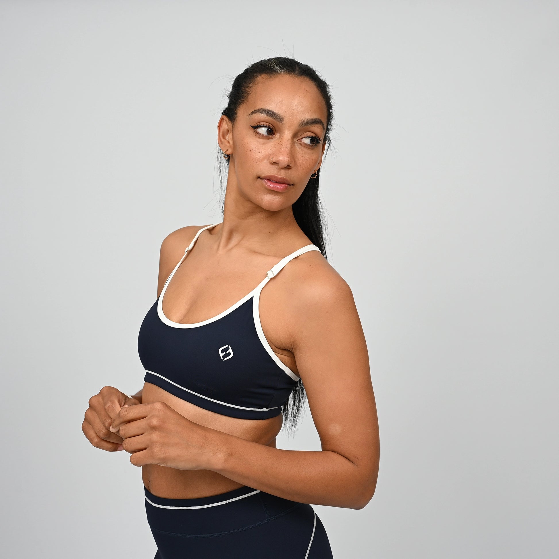 Female crossfit athlete wearing a Hybryd navy minimal sports bra with white adjustable straps against a grey background