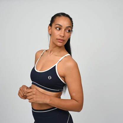 Female crossfit athlete wearing a Hybryd navy minimal sports bra with white adjustable straps against a grey background