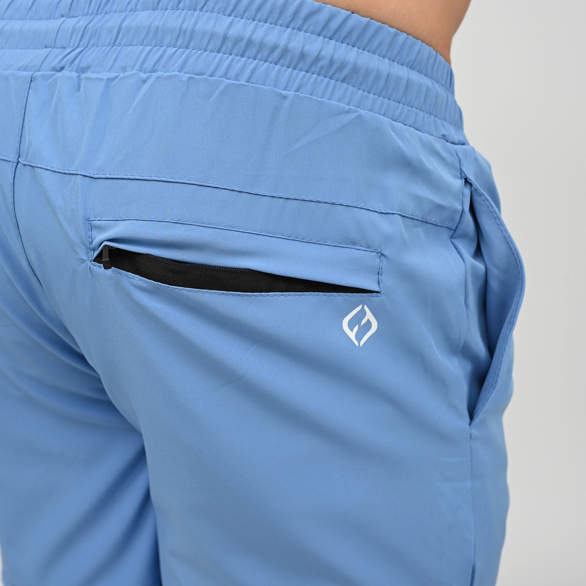 Close-up of a person wearing light blue athletic Hybryd shorts, showing the back pocket with a black interior lining and a small white Hybryd logo on the side.