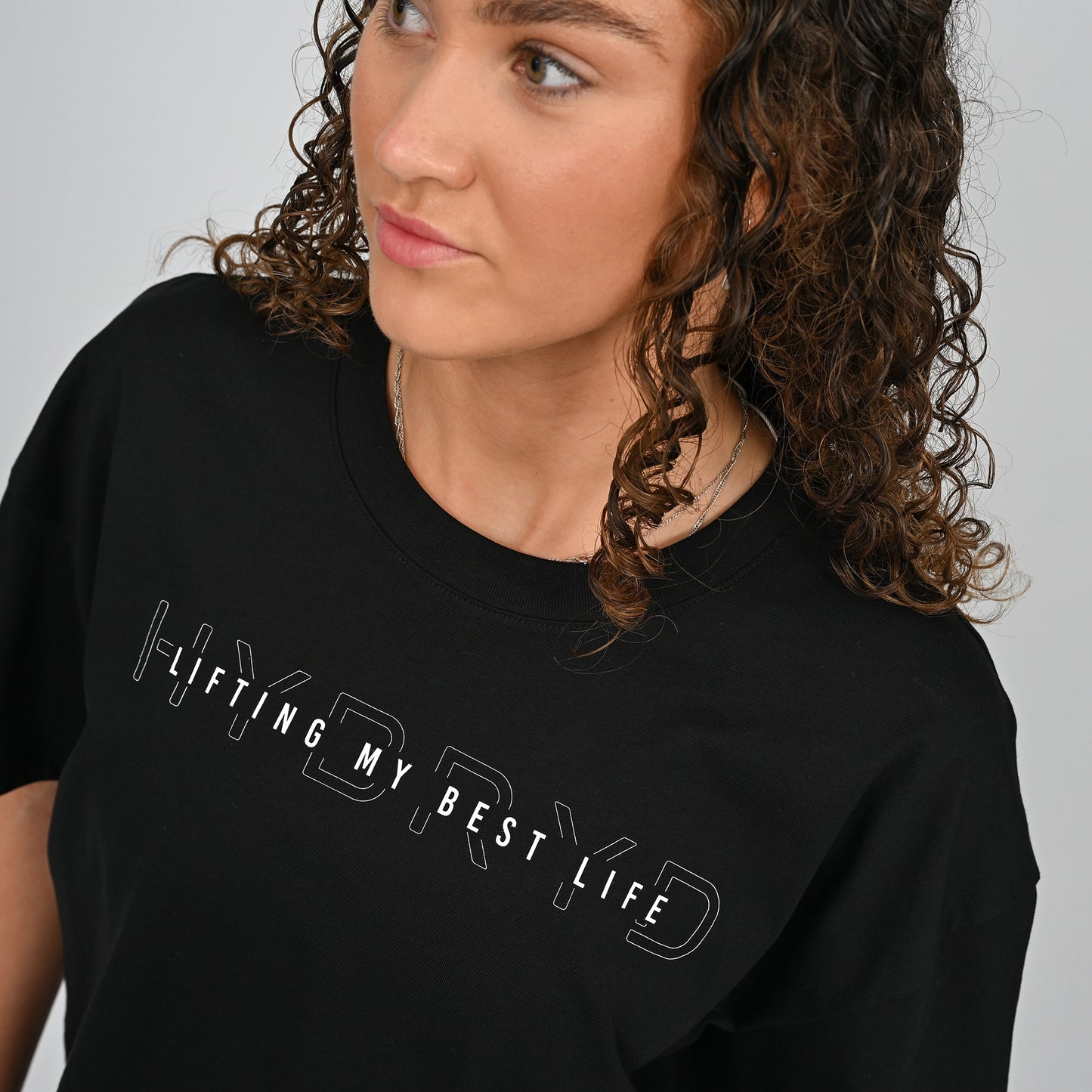 Person wearing a black t-shirt with 'HYBRYD LIFTING MY BEST LIFE' text on a plain background