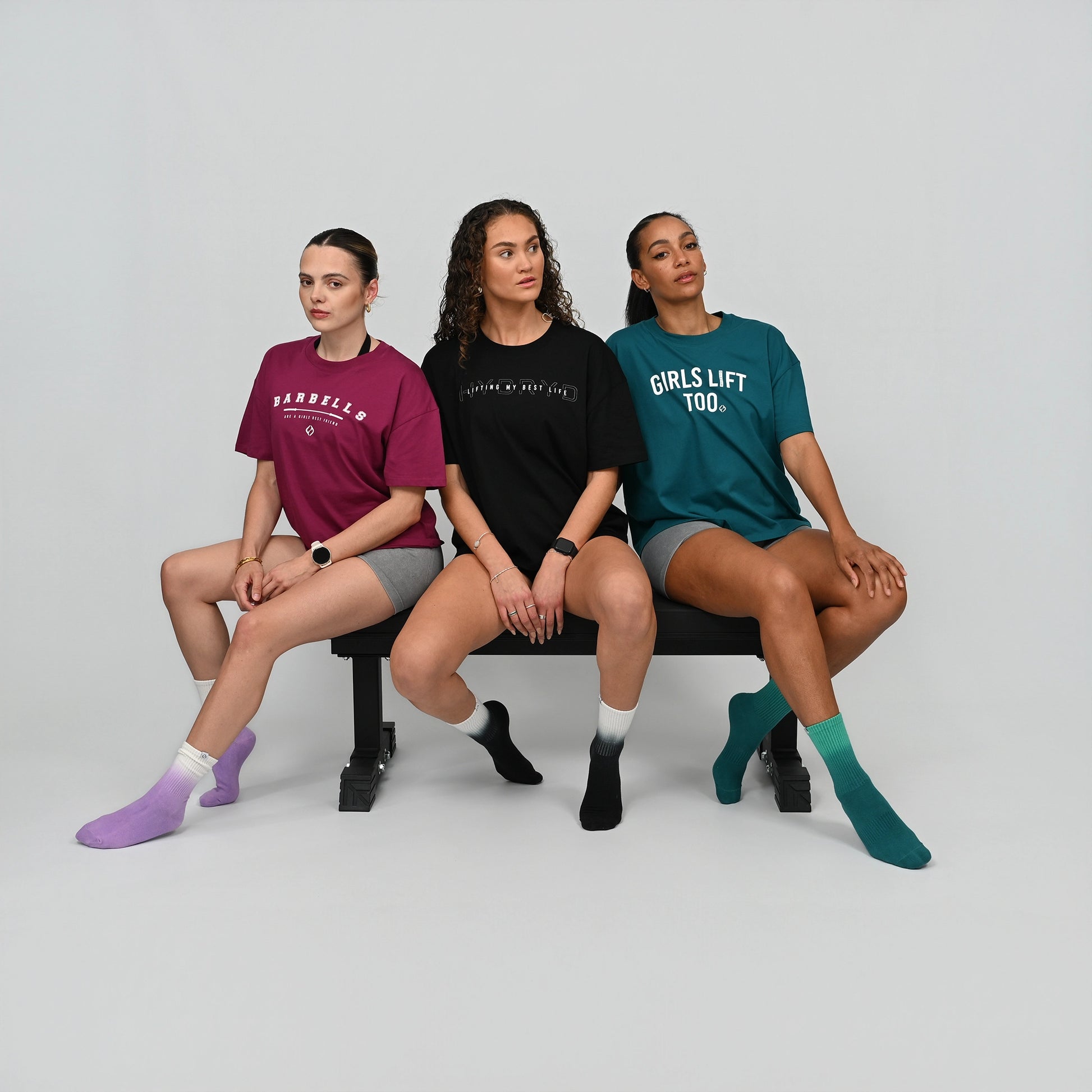 Three women sitting on a bench wearing t-shirts from the activewear brand Hybryd