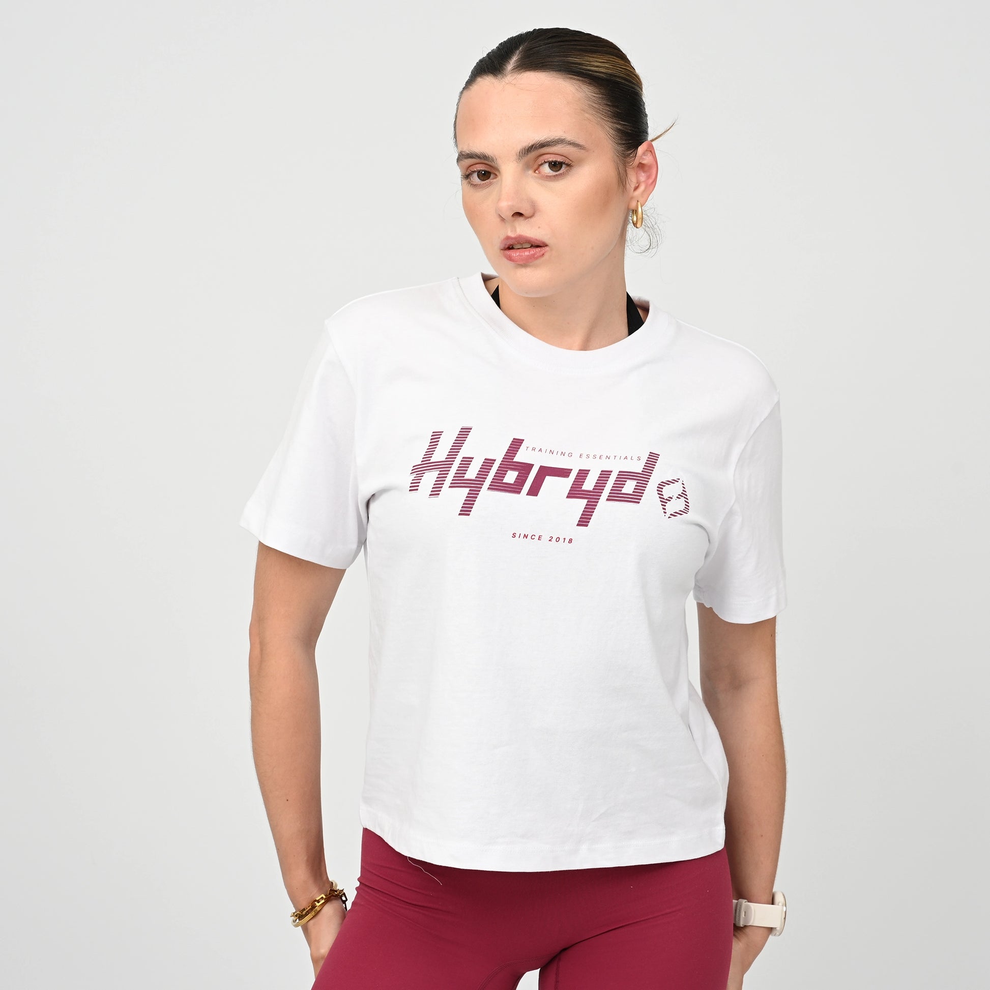 Woman wearing a boxy white t-shirt with 'Hybryd' logo on a plain background