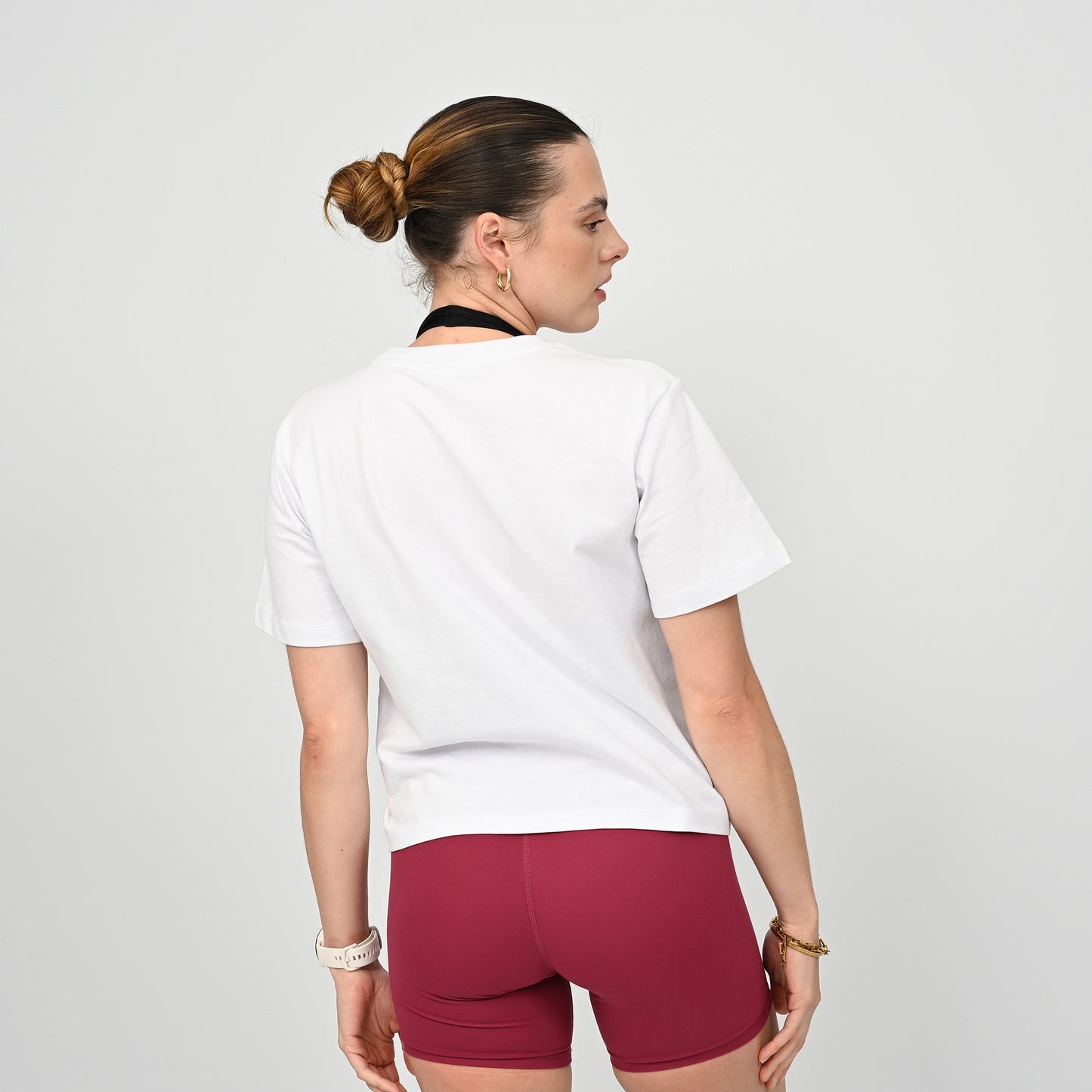 Woman wearing a white cotton  t-shirt and maroon gym shorts on a plain background