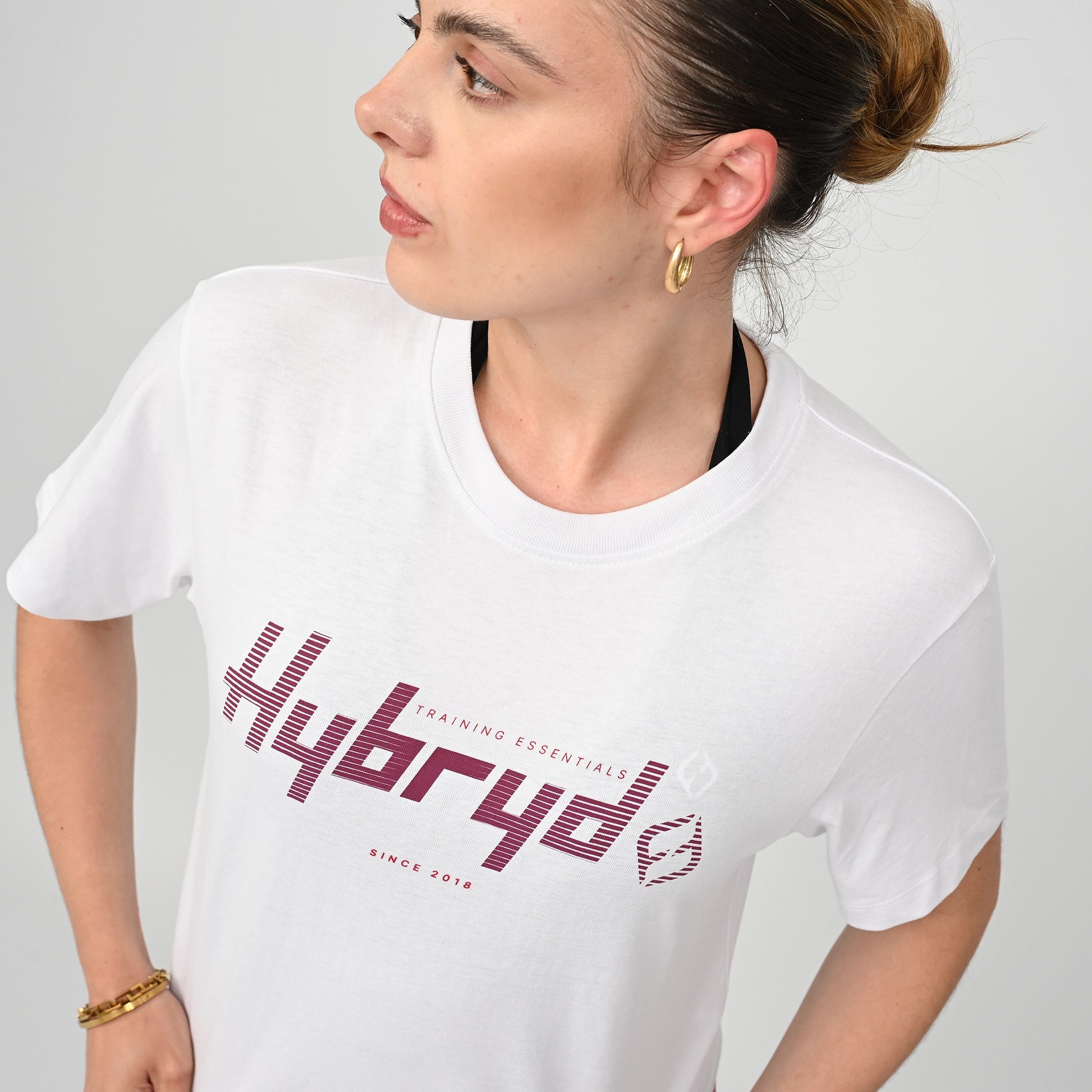 Woman wearing a white training  t-shirt with 'Hybryd' logo on a plain background