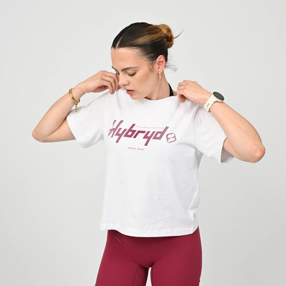 Person wearing a white gym  t-shirt with 'Hybryd' logo and red leggings on a light gray background