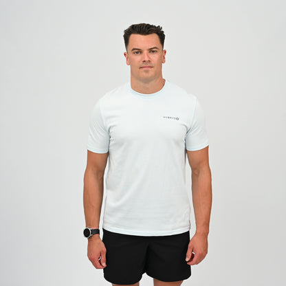 A man wearing a light blue crew-neck t-shirt with a small black Hybryd logo on the left chest, paired with black athletic shorts, standing against a light gray studio background. From Gymwear brand Hybryd.