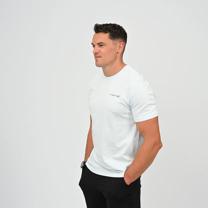 A CrossFit athlete wearing a light blue crew-neck t-shirt with a small black Hybryd logo on the left chest, paired with black athletic shorts, standing against a light gray studio background. From Gymwear brand Hybryd.