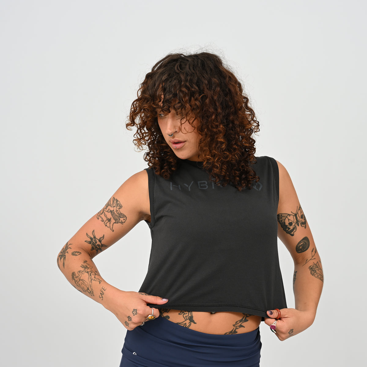 A woman wearing a HYBRYD Zara women’s black cropped gym tank vest in enzyme-washed organic cotton, relaxed fit sleeveless training top for HYROX and functional fitness.