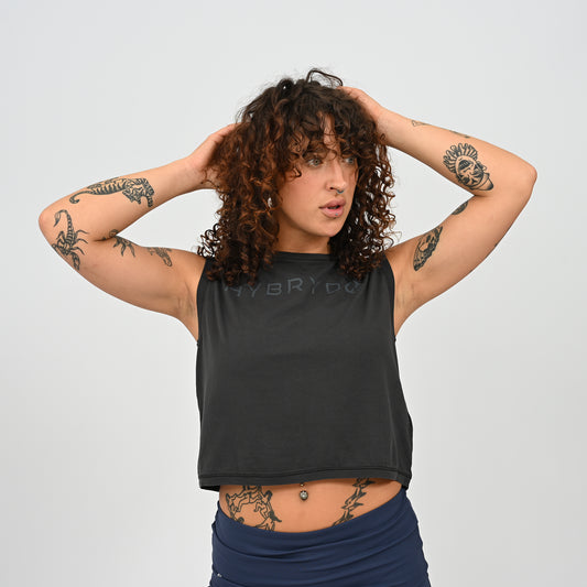 A woman wearing a HYBRYD Zara women’s black cropped gym tank vest in enzyme-washed organic cotton, relaxed fit sleeveless training top for HYROX and functional fitness.