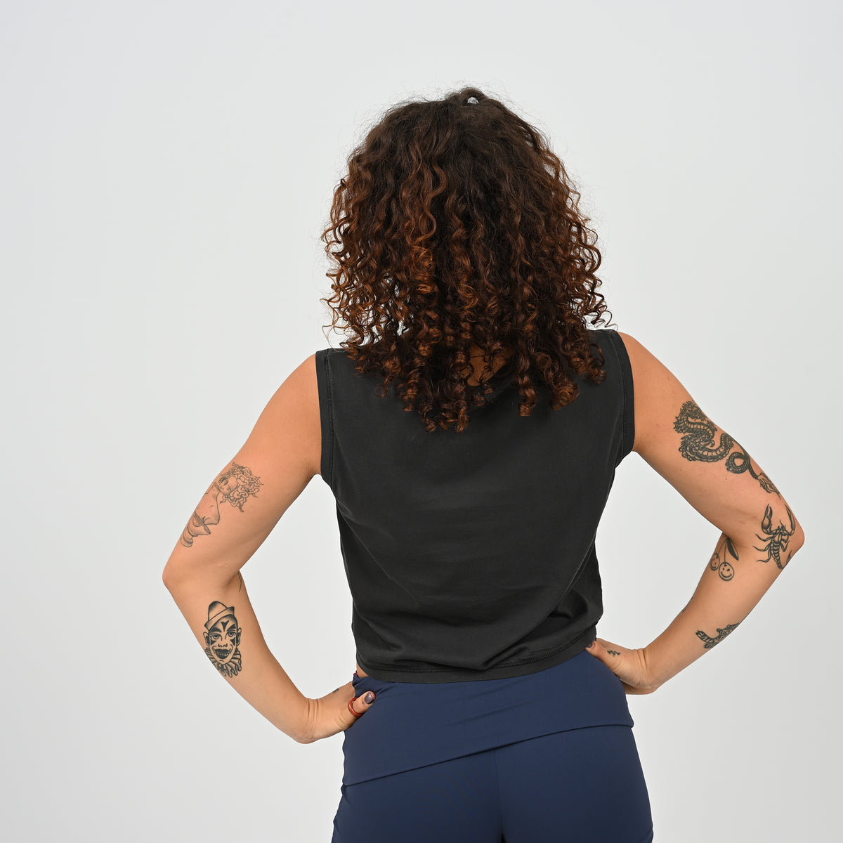 A woman wearing a HYBRYD Zara women’s black cropped gym tank vest in enzyme-washed organic cotton, relaxed fit sleeveless training top for HYROX and functional fitness.
