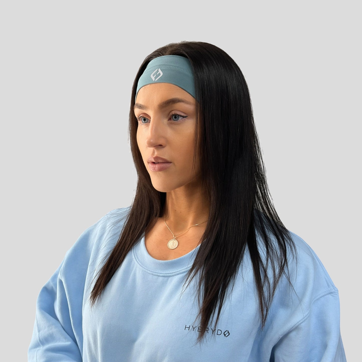 Woman wearing a light blue Hybryd headband and sweatshirt with a logo on a gray background