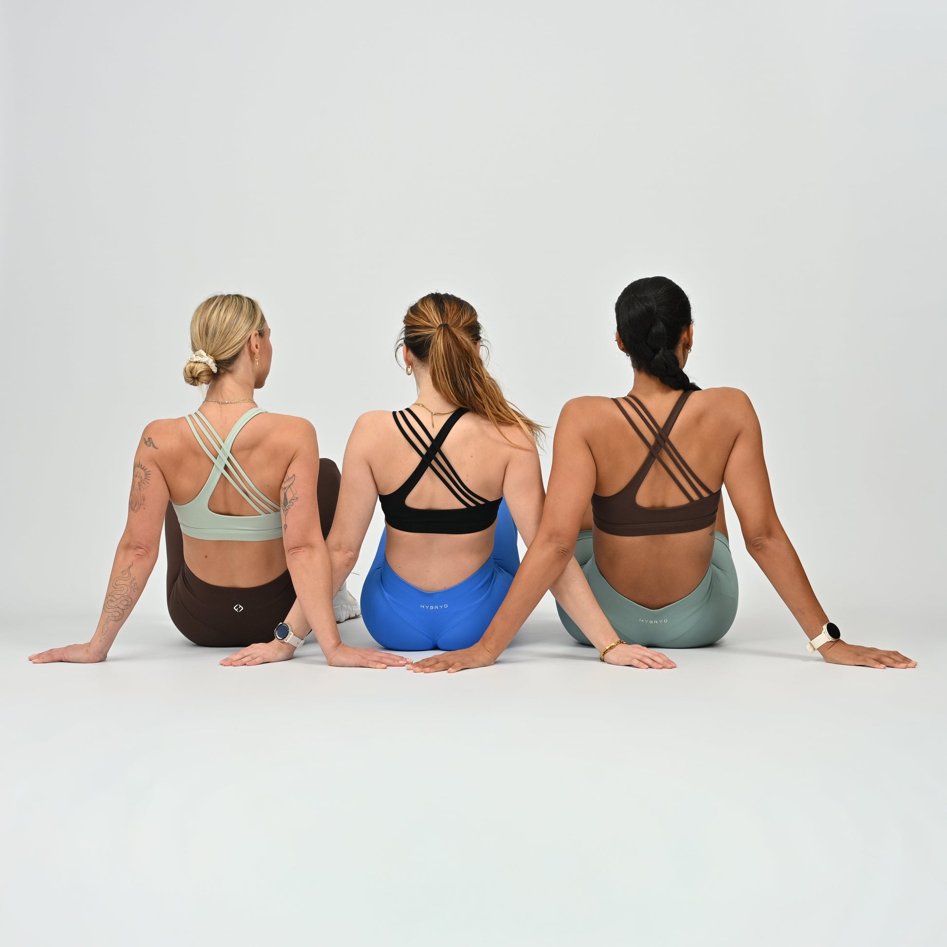 Three women sitting on the floor wearing Hybryd athletic bras