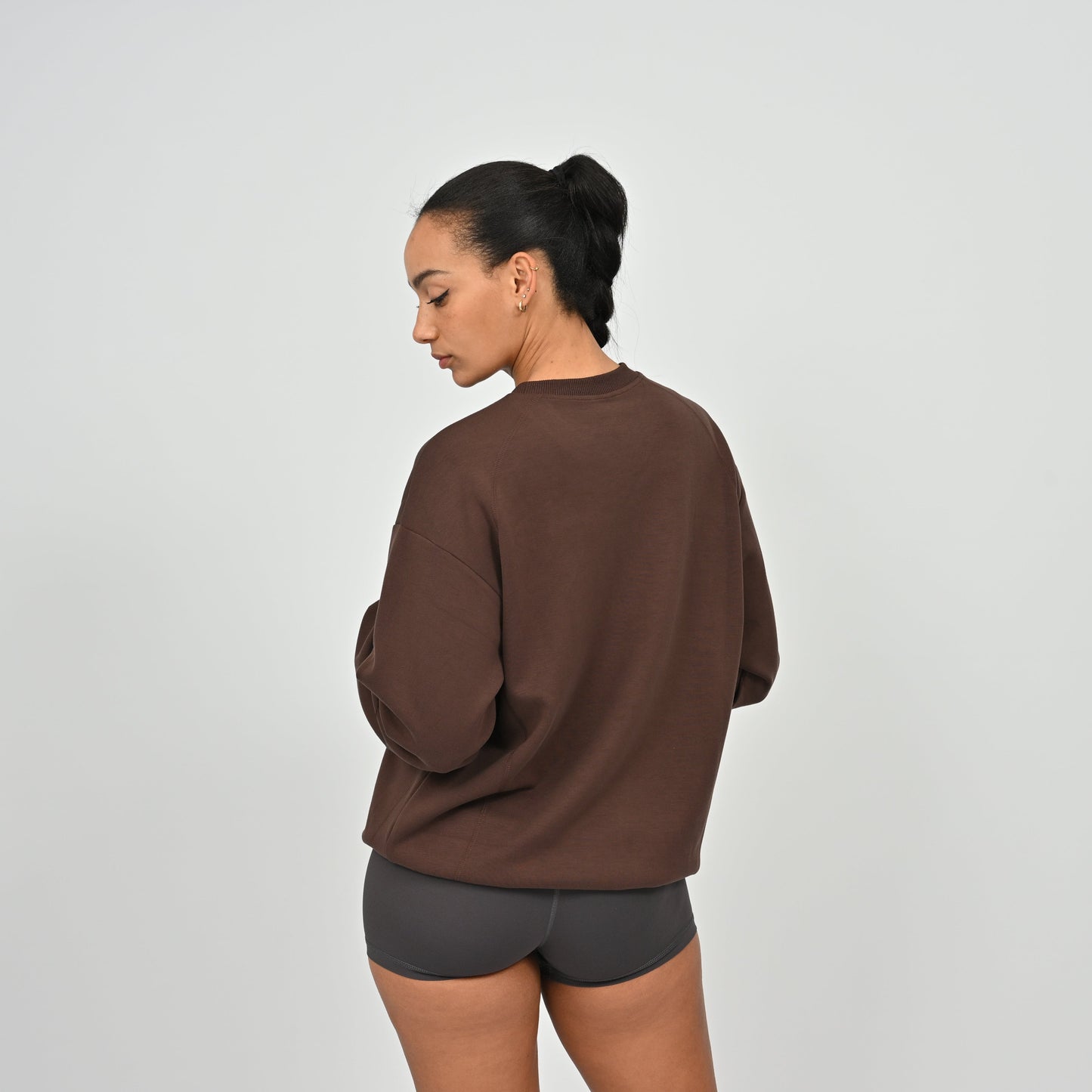 Person wearing a brown gymwear sweatshirt and gray shorts on a light gray background from brand Hybryd