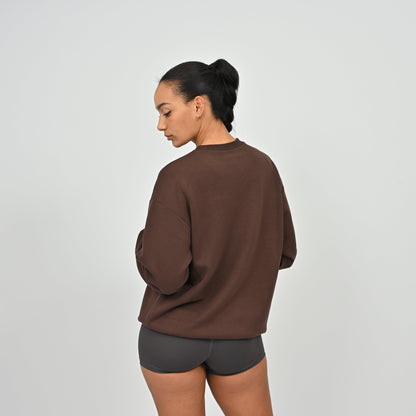 Person wearing a brown gymwear sweatshirt and gray shorts on a light gray background from brand Hybryd