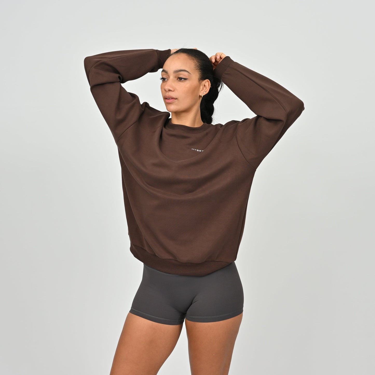 Woman wearing a brown sweatshirt and black shorts from Hybryd on a light gray background