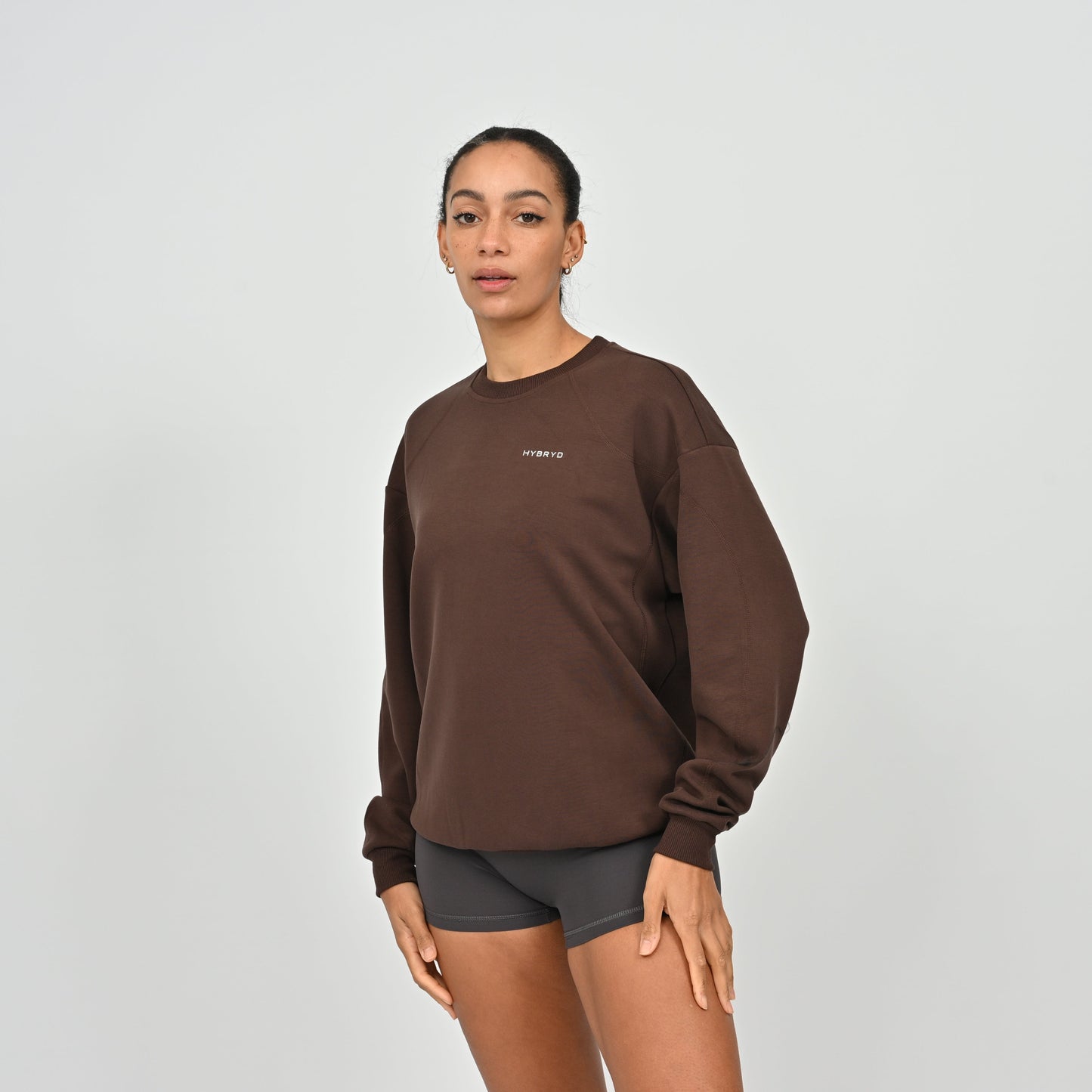 Person wearing a brown sweatshirt with a Hybryd logo on a light gray background