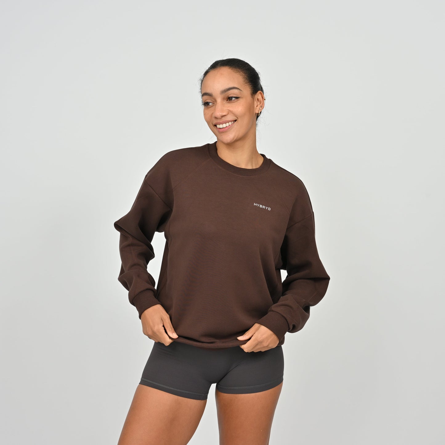 Woman wearing a brown sweatshirt and black shorts from Hybryd gymwear on a light gray background
