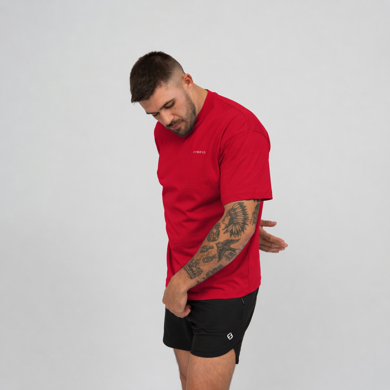 Man wearing a red t-shirt and black shorts from the brand Hybryd on a light grey background