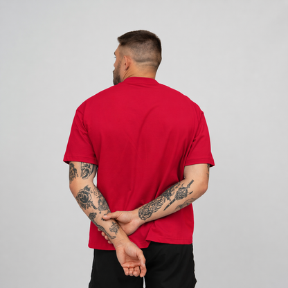 Man wearing a red Hybryd T- shirt with tattoos on arms against a grey background