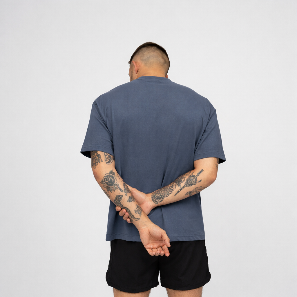 Person wearing a blue t-shirt and black shorts with tattoos on arms, standing against a plain background