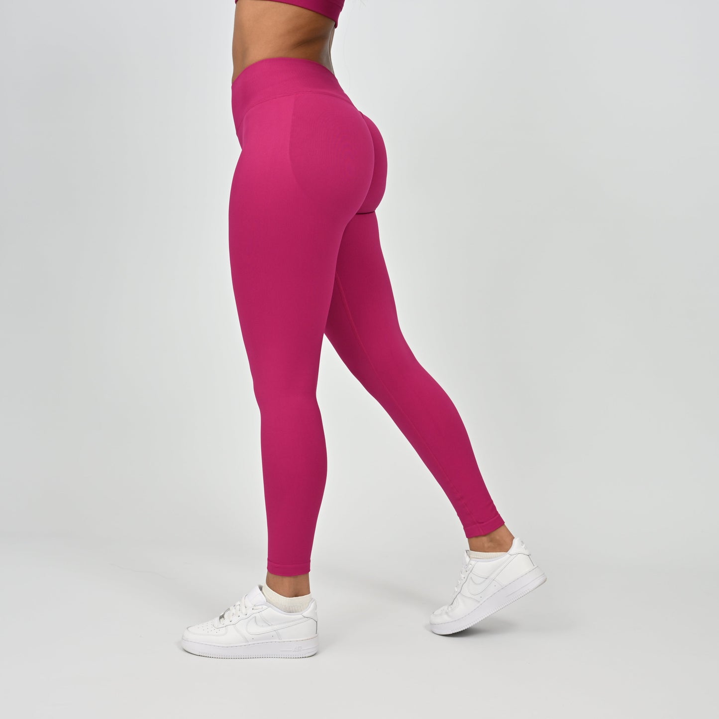 Person wearing bright pink Hybryd leggings and white sneakers on a light gray background