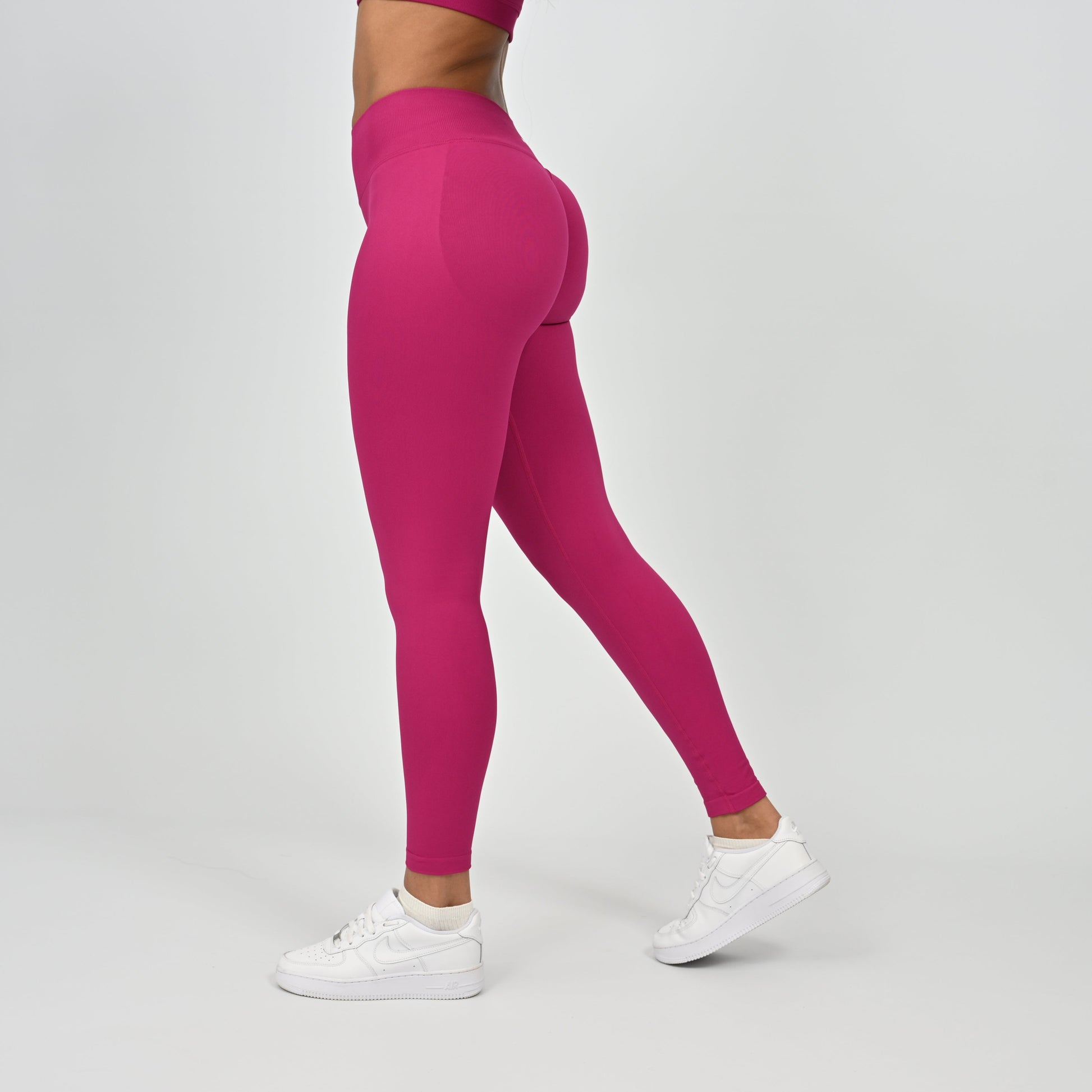 Person wearing bright pink Hybryd leggings and white sneakers on a light gray background